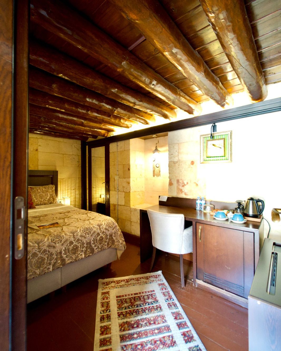 Una stanza con un letto, una scrivania, una sedia, un angolo cottura e un tappeto decorato.
