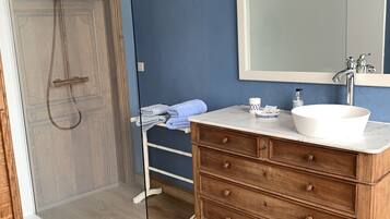 A bathroom with a glass shower enclosure, a wooden vanity with a white sink, and a large mirror.