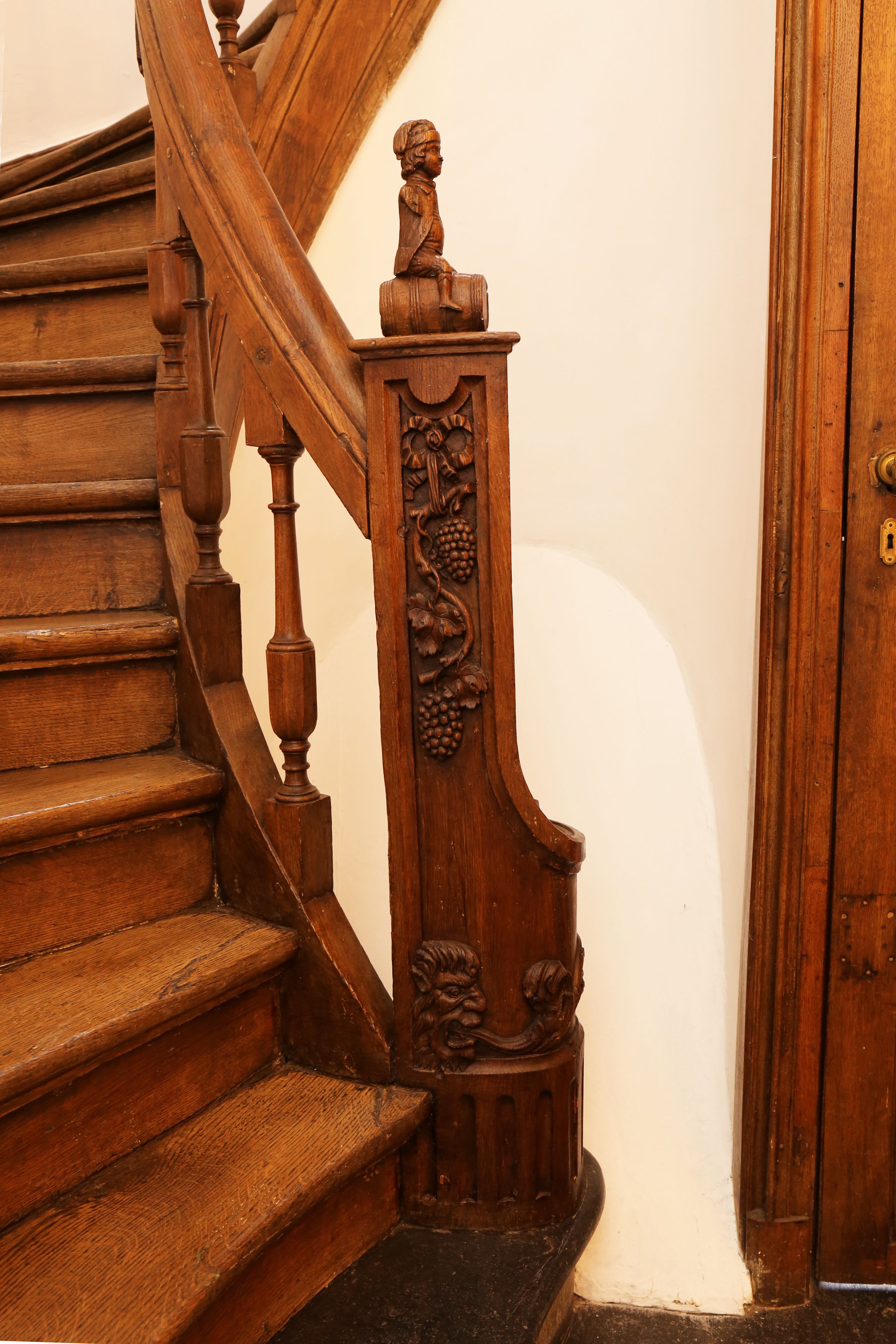 A wooden staircase with intricate carvings and a door with a brass handle.