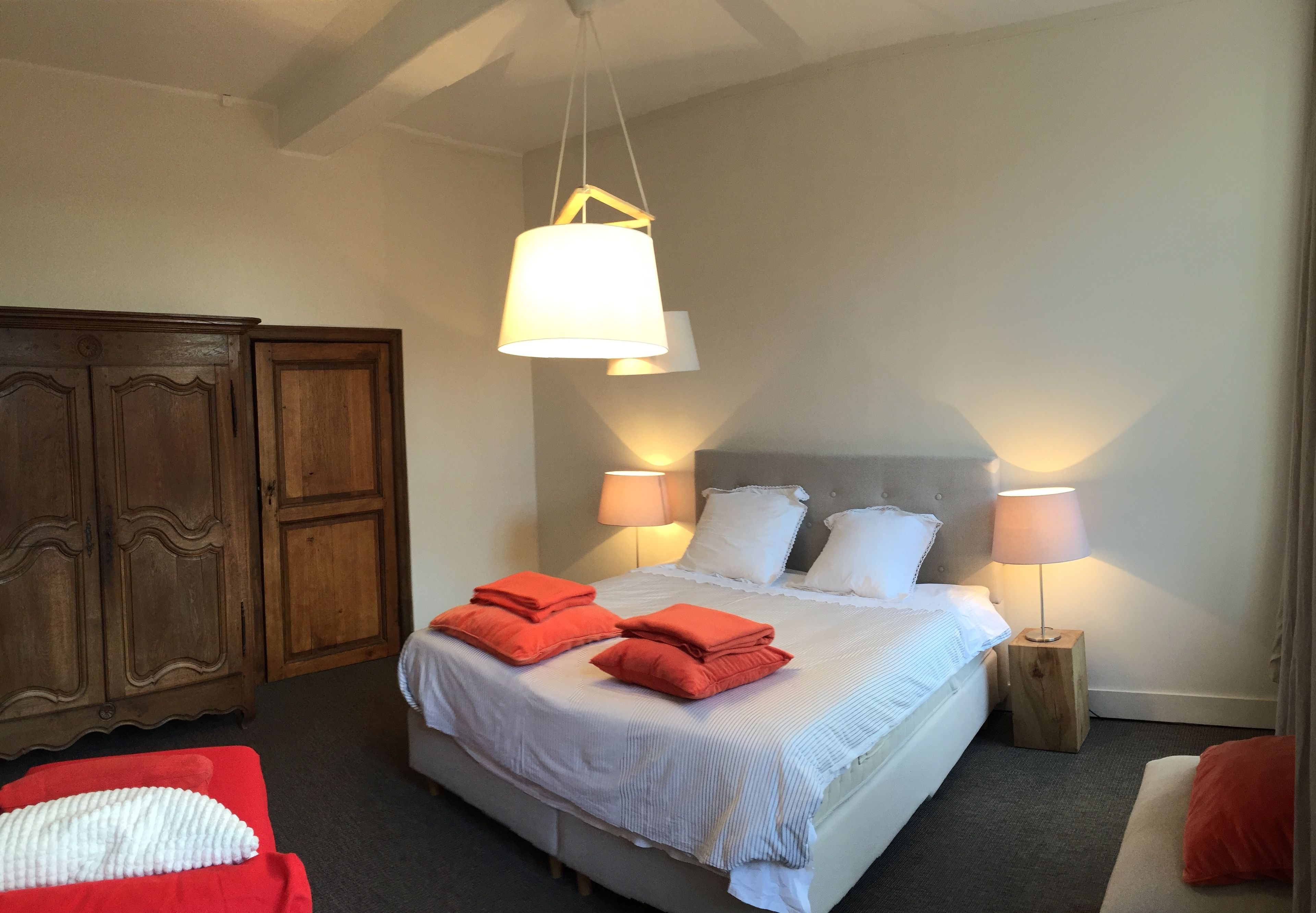 A neatly made bed with white and red linens, two bedside lamps, and a wooden wardrobe.