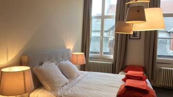 A hotel room with a bed, two bedside lamps, a window with curtains, and a radiator.