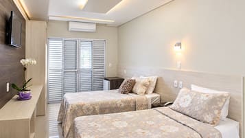A hotel room with two beds, a TV, an air conditioner, and a small table with a plant.