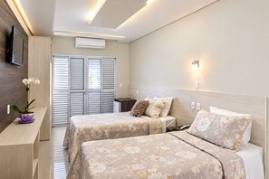 A hotel room with two beds, a TV, an air conditioner, and a small table with a plant. - Tezla Hotel (Primavera do Leste)