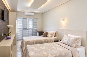 Habitación de hotel con dos camas, televisión, aire acondicionado y una mesita con una planta.