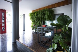 Um espaço interno moderno com piso de madeira, uma mesa de vidro e diversos vasos com plantas.