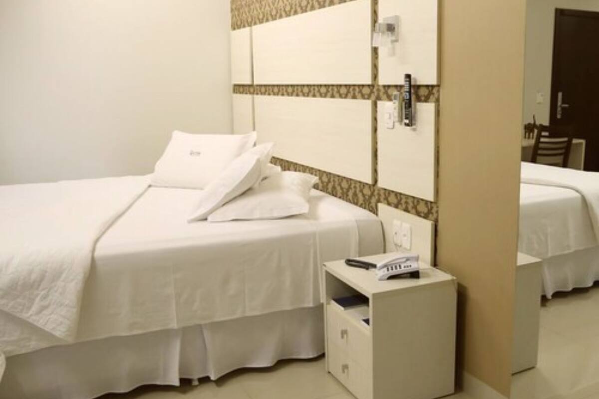 A hotel room with a bed, a bedside table, a mirror, and a wall with a patterned design.