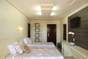 Quarto de hotel moderno com duas camas, uma televisão de tela plana na parede, uma escrivaninha pequena e uma orquídea em vaso.