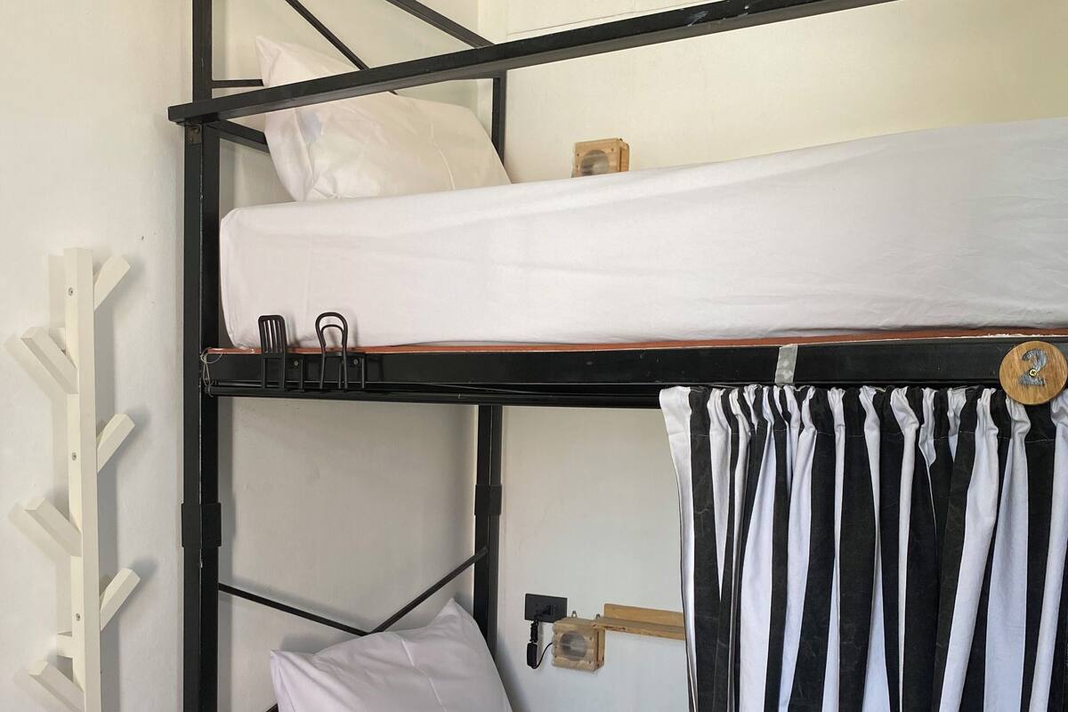 A bunk bed with a white mattress and pillows, a wooden headboard, and a black metal frame.