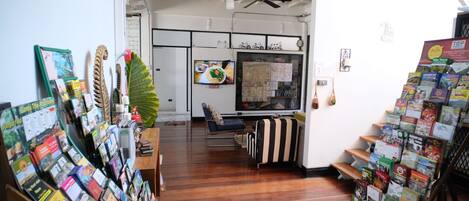 A room with wooden flooring, a ceiling fan, a television, and a window with a map.