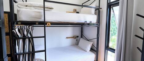 Quarto com beliche, janela, piso de madeira e grade de metal.