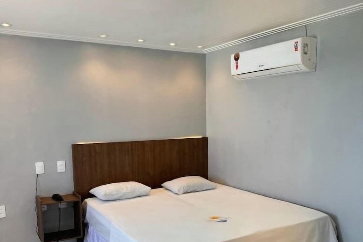 A single-bed room with a wooden headboard, a bedside table, and a wall-mounted air conditioning unit.