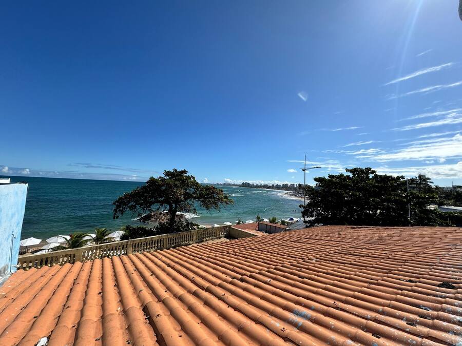 A rooftop terrace with terracotta tiles, overlooking a coastal area with a clear sky and calm sea.