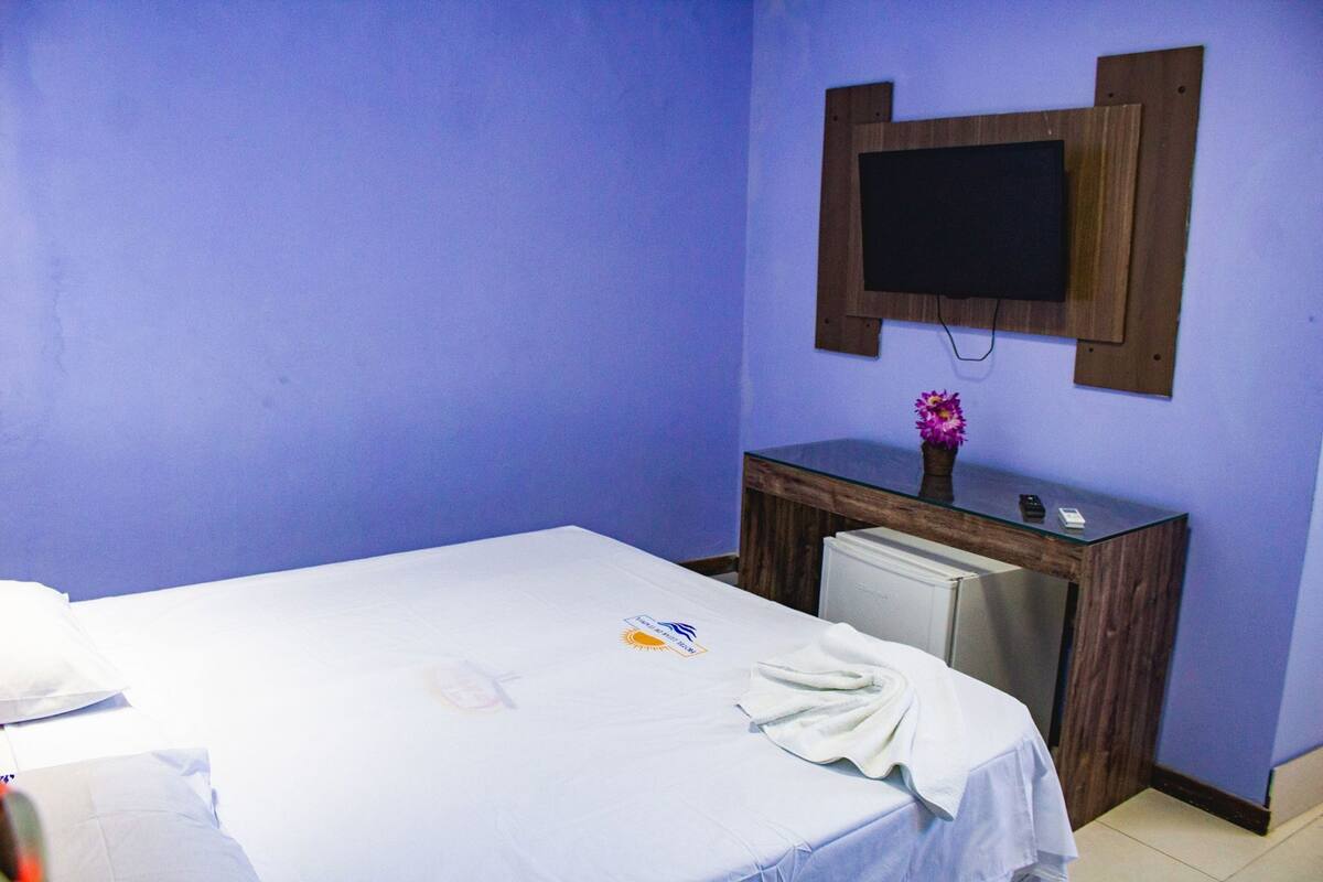 A room with a bed, a desk, a chair, a small refrigerator, and a television mounted on the wall.
