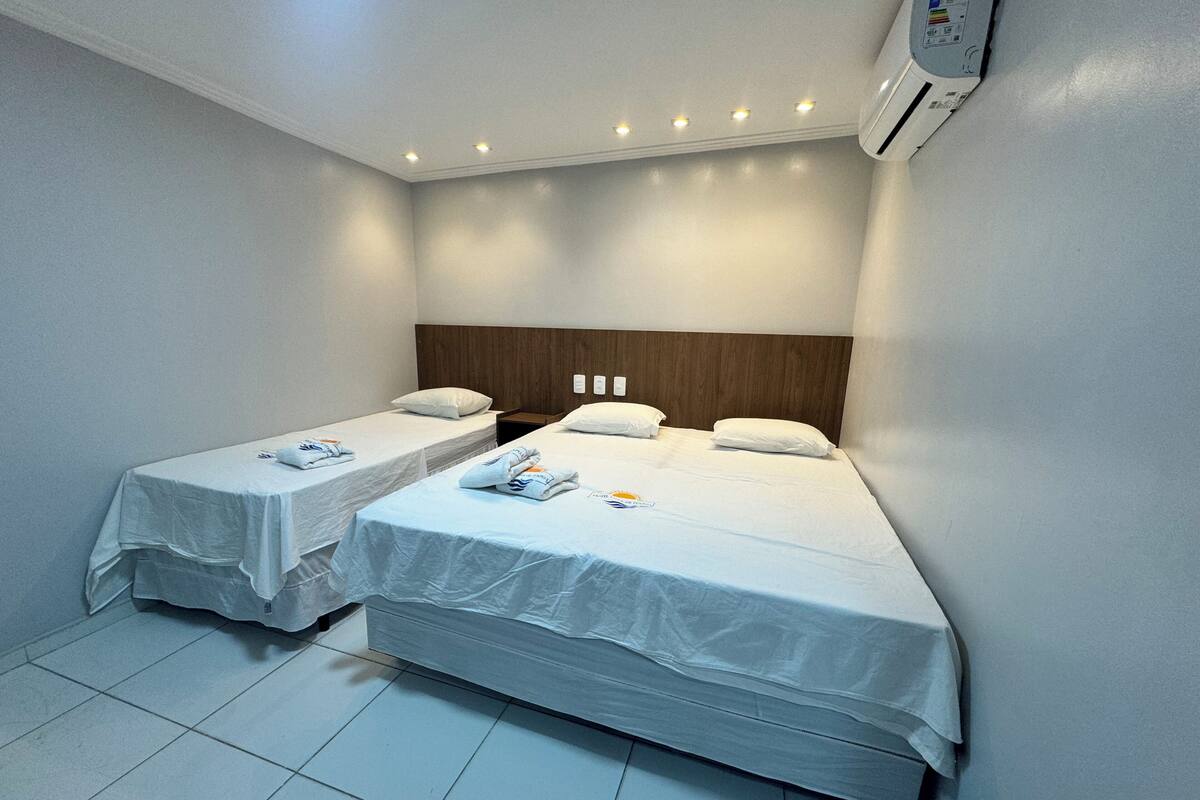A hotel room with two single beds, a wooden headboard, and an air conditioning unit.
