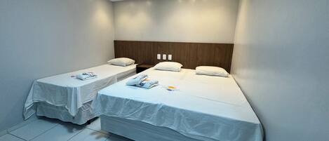Habitación de hotel con dos camas individuales, cabecero de madera y aire acondicionado.