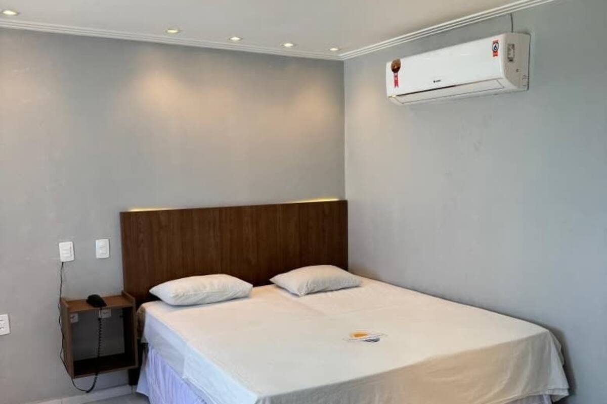 A bedroom with a single bed, a wooden headboard, a bedside table with a phone, and a wall-mounted air conditioner.