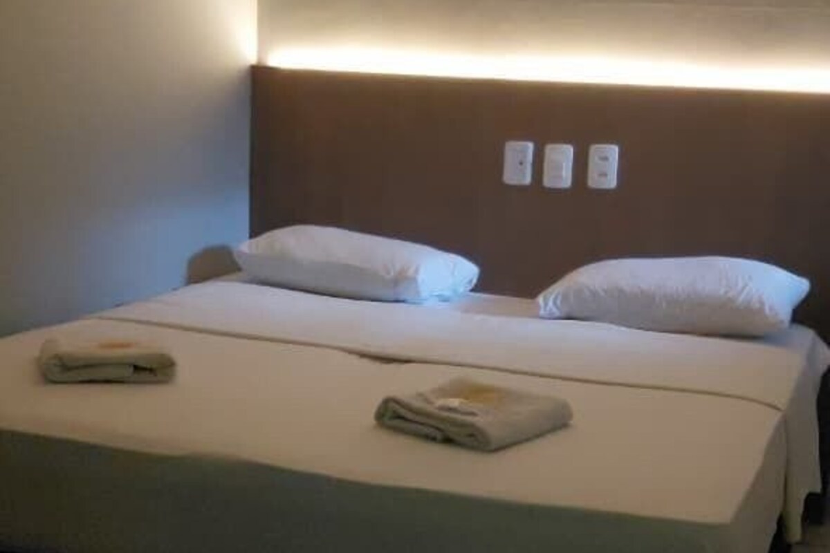 A hotel room with a bed, a headboard with built-in lighting, and a wall-mounted control panel.