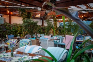 An outdoor patio area with wicker furniture, tables, and chairs, surrounded by greenery and string lights. - House Dublin (Dublin)