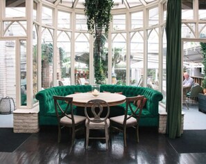 A conservatory with a green upholstered sofa, wooden chairs, and a round table. - House Dublin (Dublin)