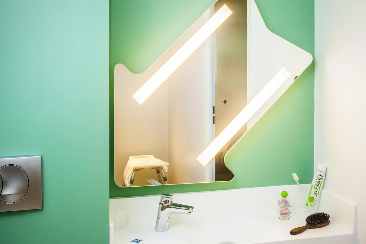 Un baño con una pared verde, un lavabo blanco, un espejo, un cepillo de dientes, un tubo de pasta de dientes y un cepillo para el pelo.