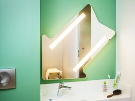 Un baño con una pared verde, un lavabo blanco, un espejo, un cepillo de dientes, un tubo de pasta de dientes y un cepillo para el pelo.