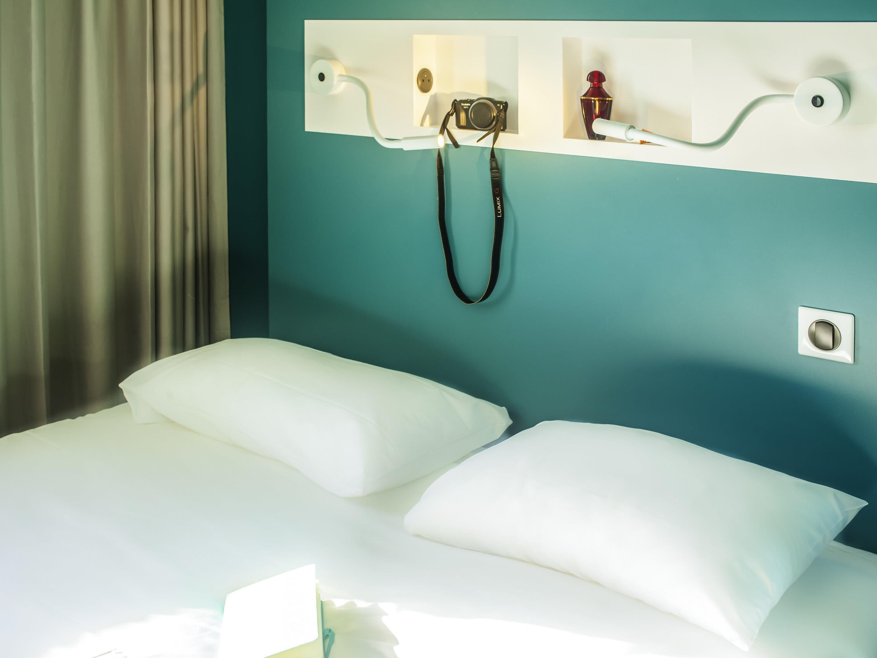 A hotel room with a bed, a wall-mounted camera, and a small bottle.