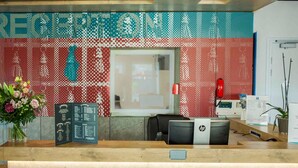 A reception desk with a patterned wall, a potted plant, and a menu board.