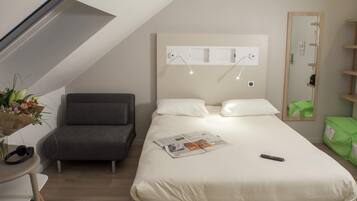 A modern hotel room with a bed, a small desk, a chair, and a mirror.
