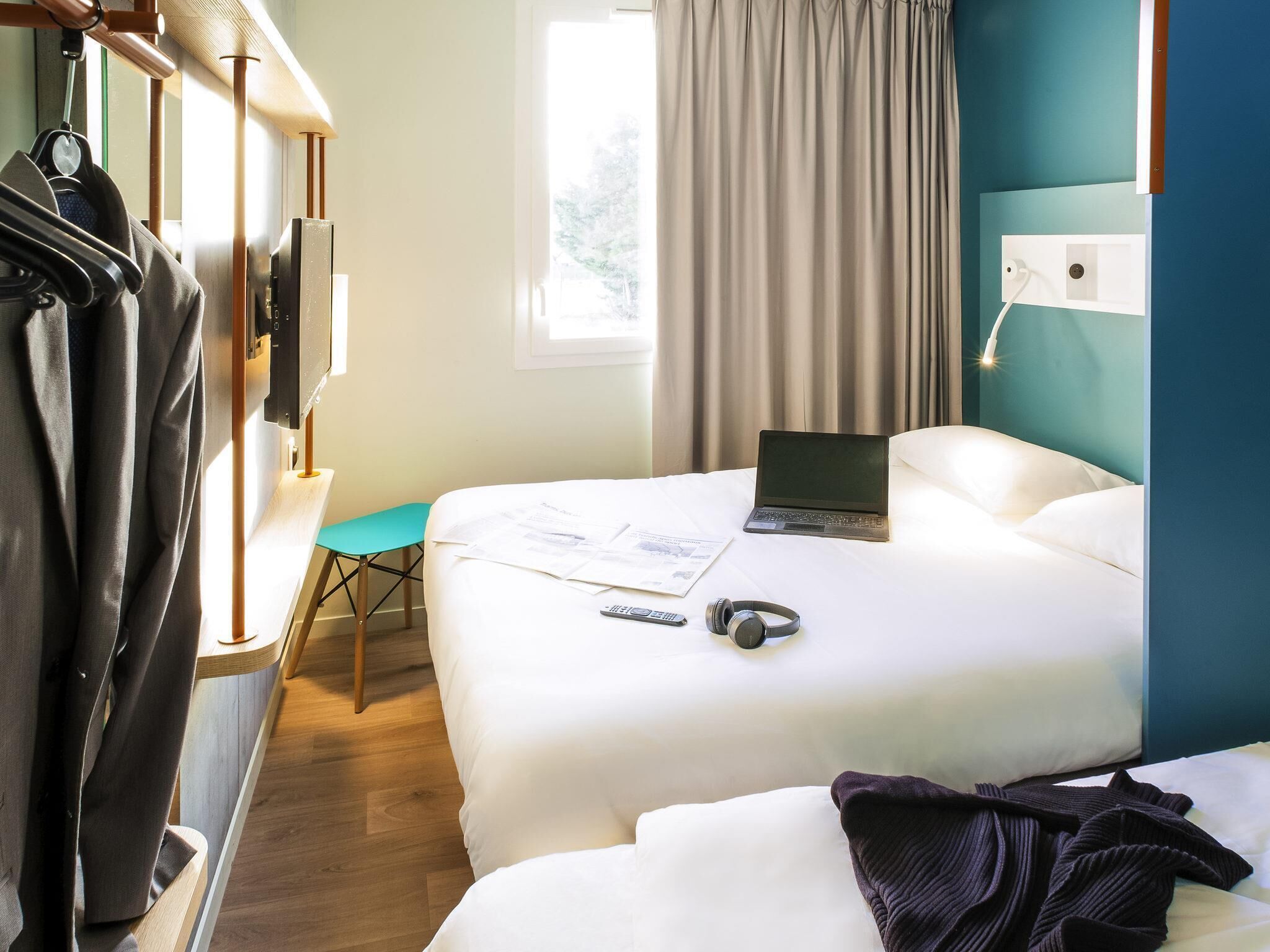 A hotel room with a bed, a laptop, a remote control, and a pair of headphones on the bed.