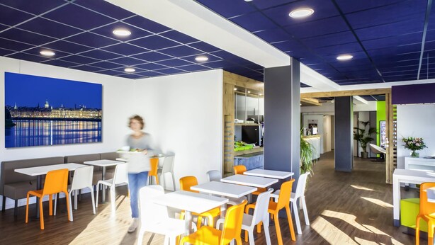 A modern dining area with tables and chairs, a cityscape painting, and a kitchen area.