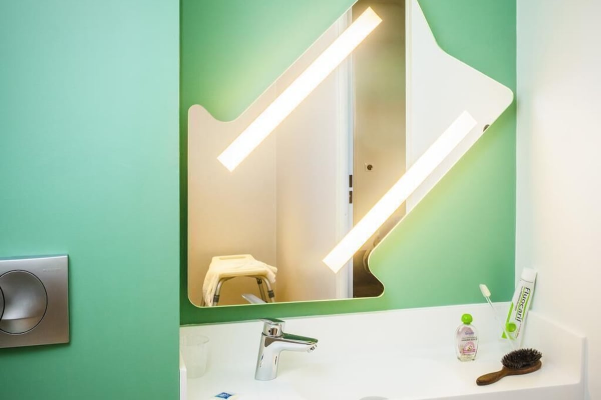 Un baño con pared verde, un lavamanos blanco, un espejo y un cepillo de dientes.