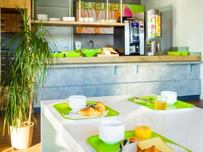 A modern kitchen with a breakfast setup including croissants, juice, and coffee. - ibis budget Bordeaux Lormont (Lormont)