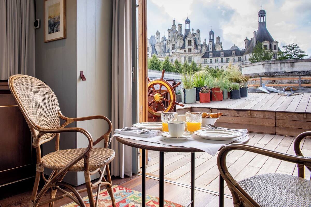 A balcony with wicker chairs, a table set for breakfast, and a view of a historic building.