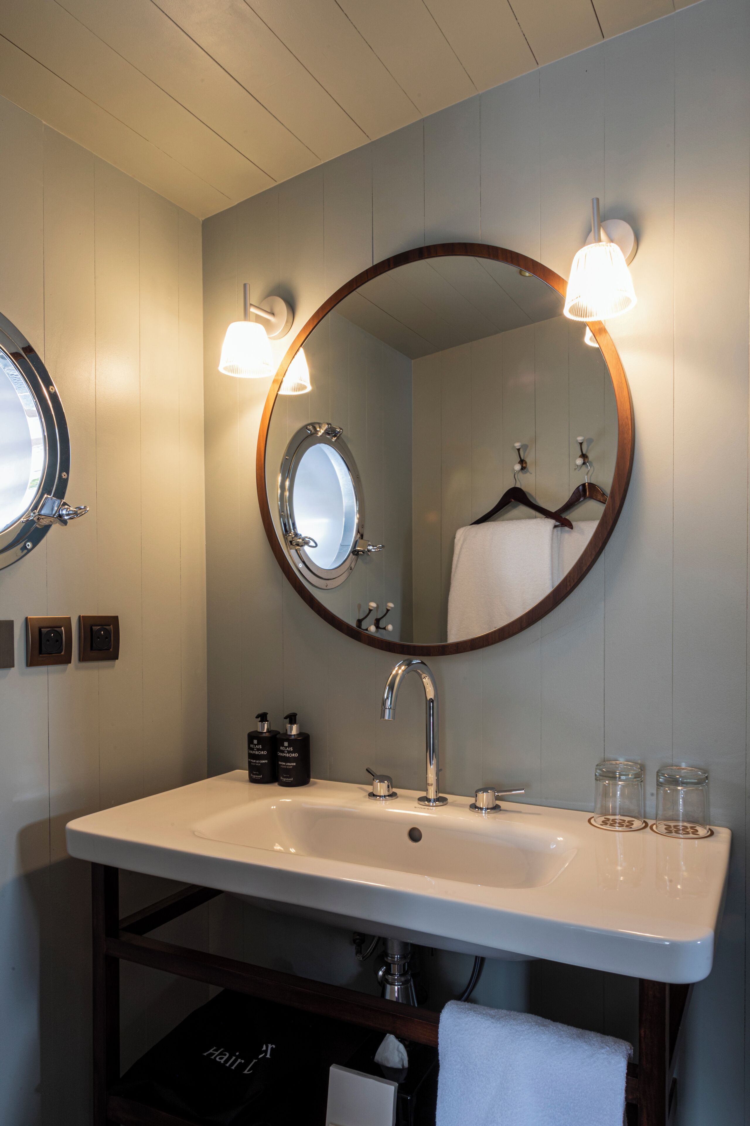 Un baño con un lavabo blanco, un espejo redondo con marco de madera y dos luces empotradas.