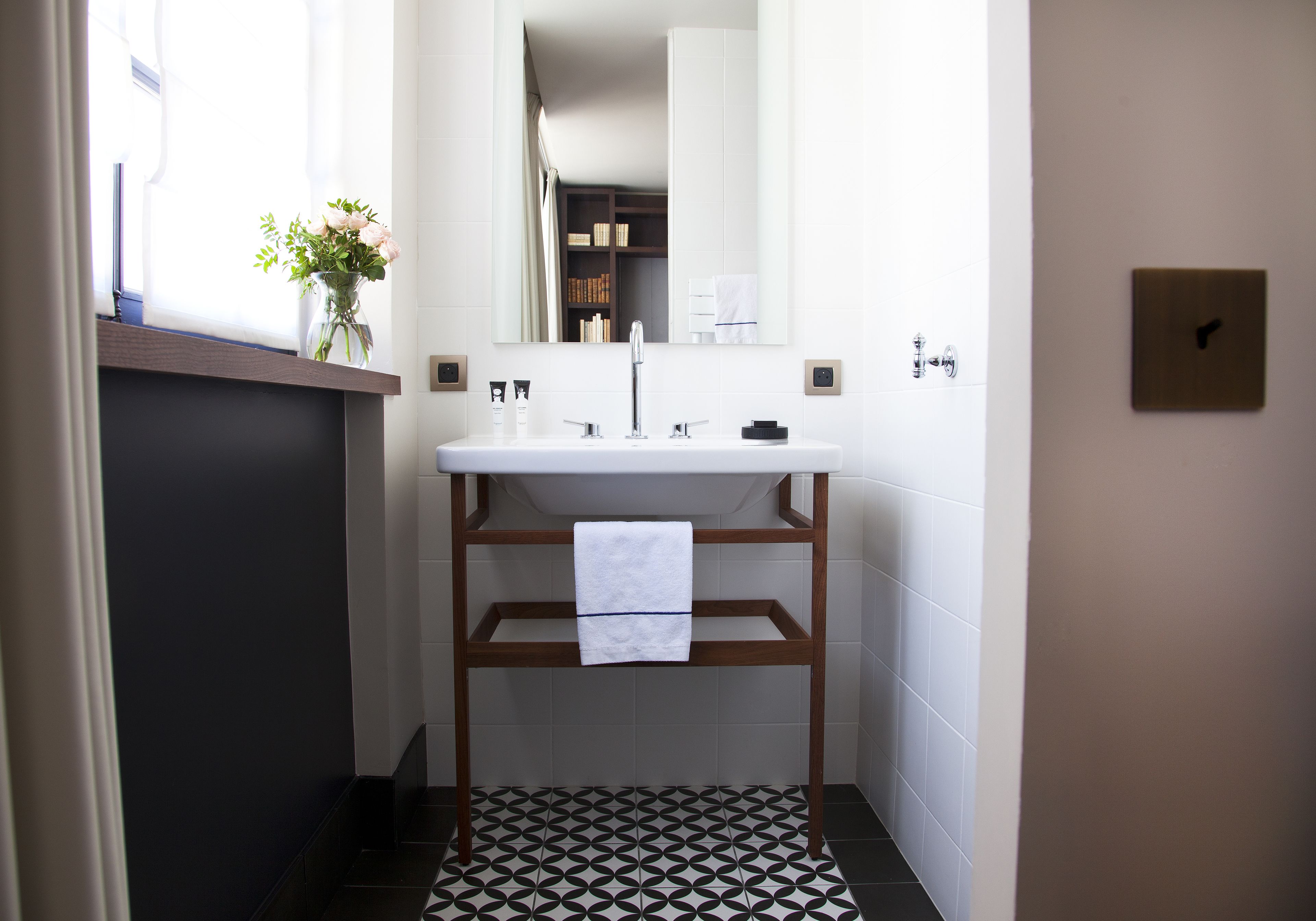 A bathroom with a white sink, a mirror, a towel rack, and a patterned floor.