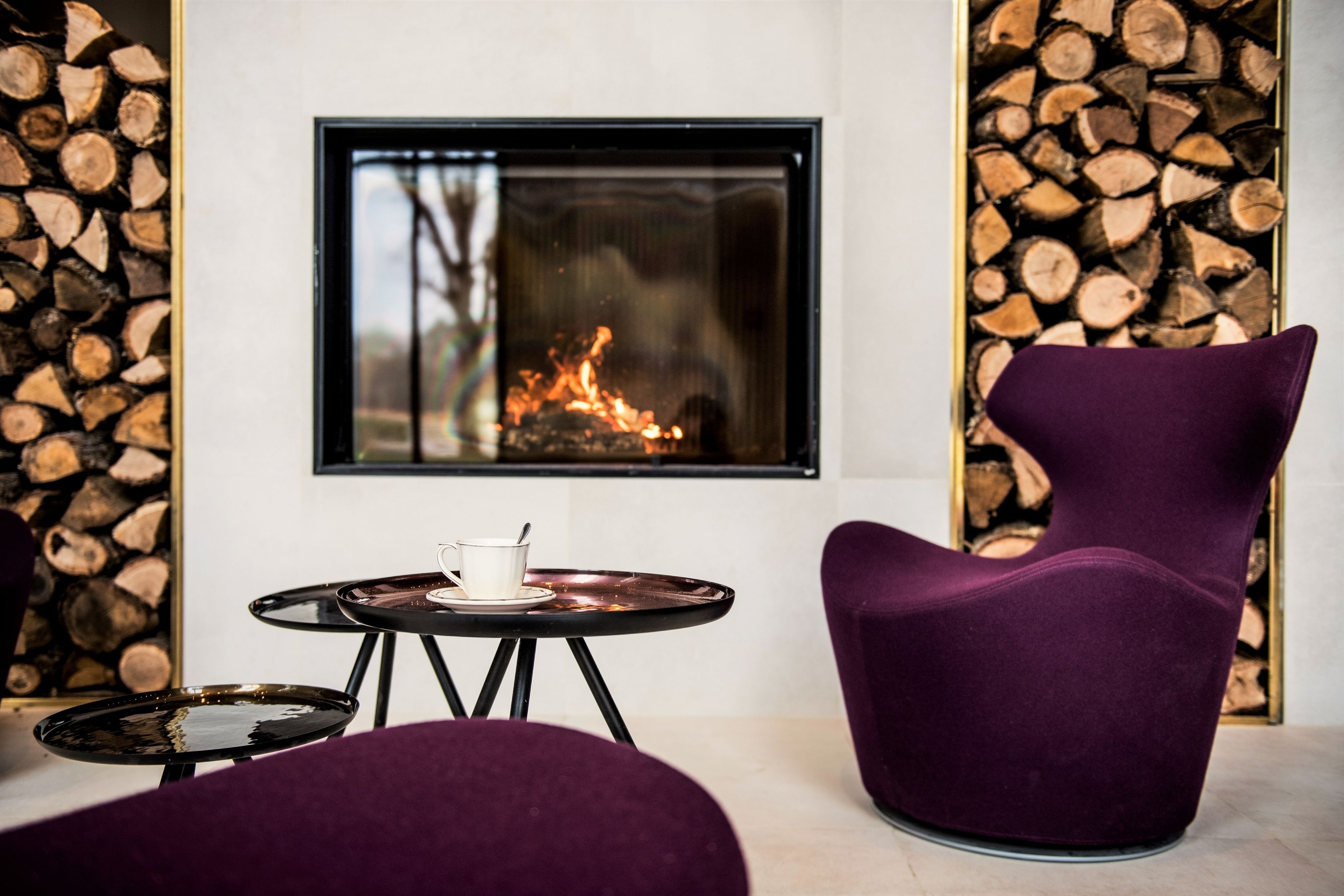 Ein moderner Raum mit Kamin, einem violetten Sessel und einem kleinen Tisch mit einer Tasse.