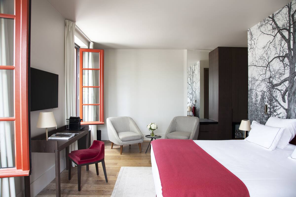 A hotel room with a bed, desk, chairs, and a TV.
