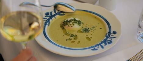 Una mesa de comedor con un plato de sopa, una copa de vino blanco y cubiertos.