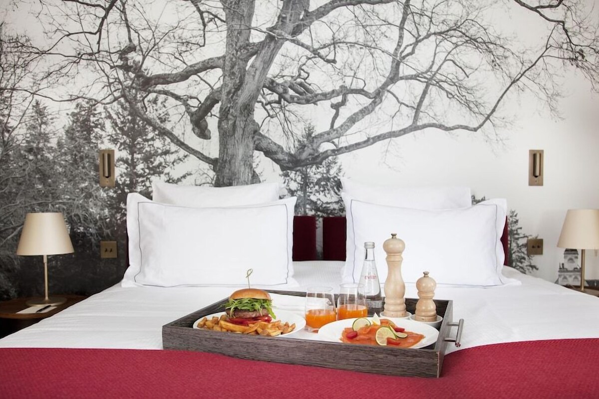 A hotel room with a bed, a tray with breakfast, a wall mural, and two lamps.