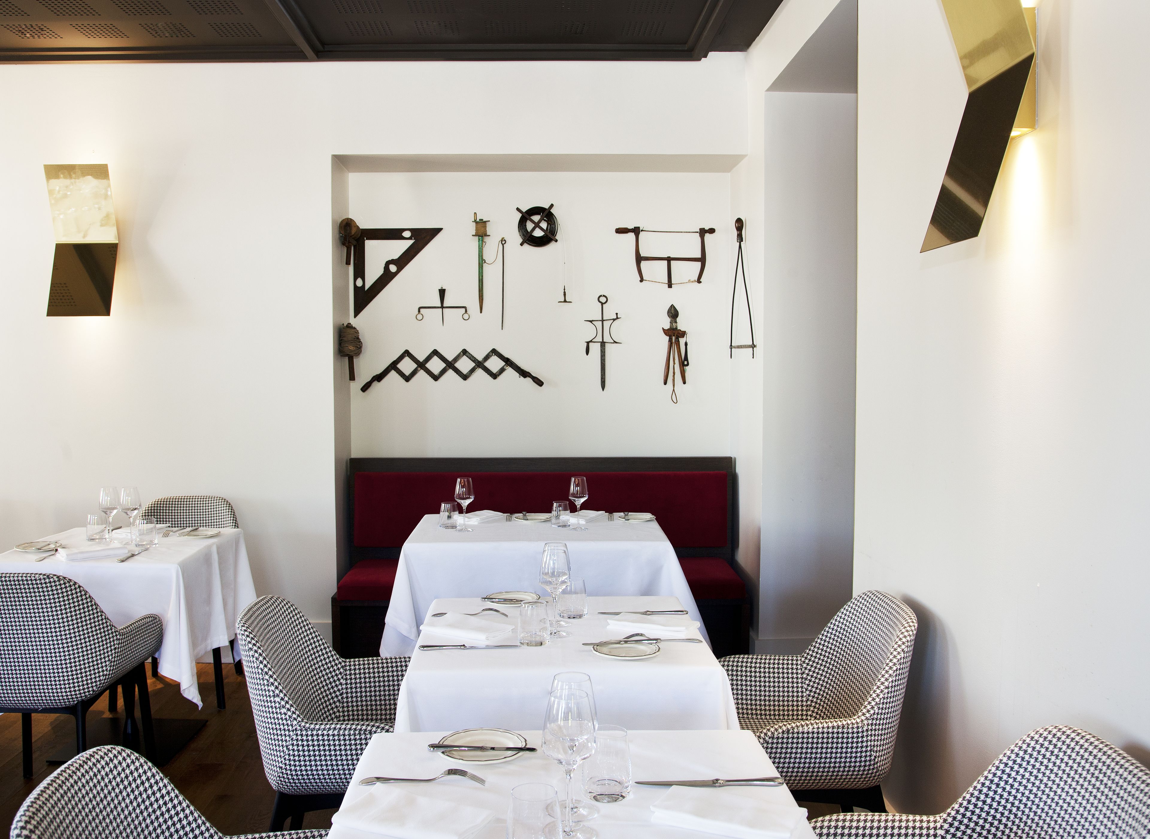 A restaurant with a long table set for dining, houndstooth patterned chairs, and a wall decorated with various tools and equipment.