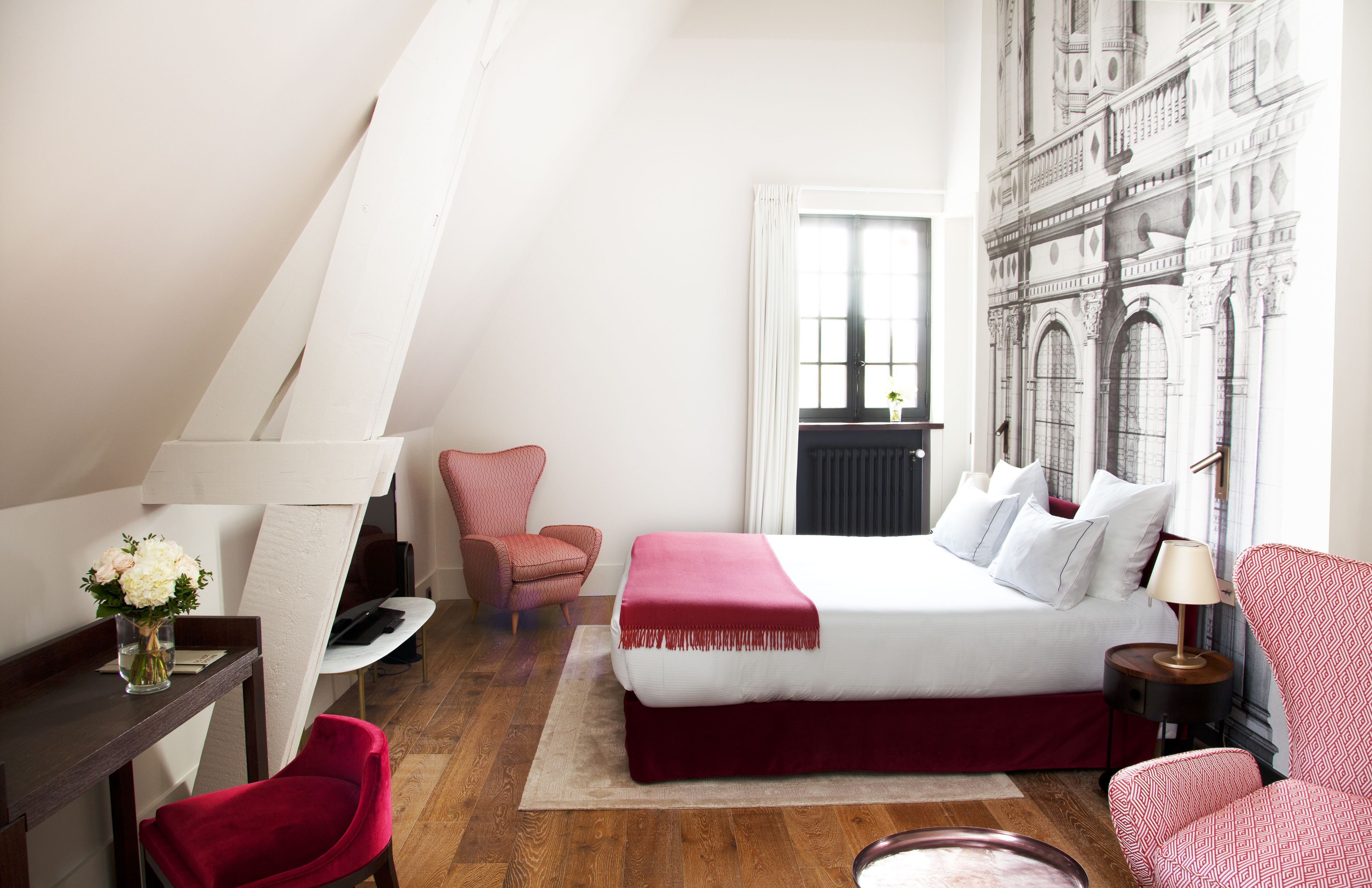 A bedroom with a bed, a desk, a chair, a lamp, and a large window.