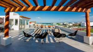 A rooftop terrace with a wooden pergola, outdoor seating, and a view of the ocean. - Splendid 1 bedroom by Happy Address (Playa del Carmen)
