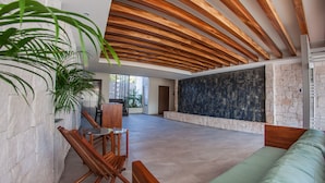 A spacious indoor area with a high ceiling featuring wooden beams, a seating area with a green sofa, a small round table, and chairs. - Splendid 1 bedroom by Happy Address (Playa del Carmen)