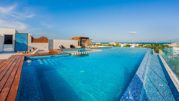 A rooftop infinity pool with a wooden deck, lounge chairs, and a view of the coastline. - Splendid 1 bedroom by Happy Address (Playa del Carmen)