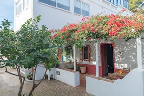 A white building with a red door, a balcony with red flowers, and a paved courtyard. - Fabrica Beach Apartamentos (Vila Real Santo Antonio)