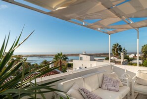 A terrace with a white sofa and armchair, overlooking a coastal view with palm trees and buildings. - Fabrica Beach Apartamentos (Vila Real Santo Antonio)