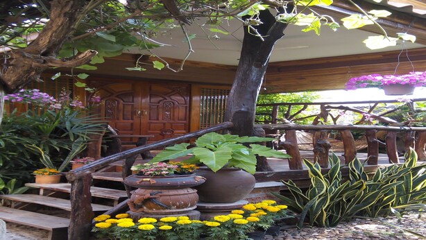 A wooden staircase leading to a porch with potted plants and flowers. - Orchid Homestay Buriram No1 (Phlapphlachai)