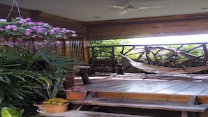 A wooden deck with a hammock, wooden benches, and potted plants. - Orchid Homestay Buriram No1 (Phlapphlachai)