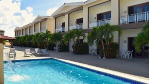 Un hotel con piscina, sillas de descanso y palmeras.