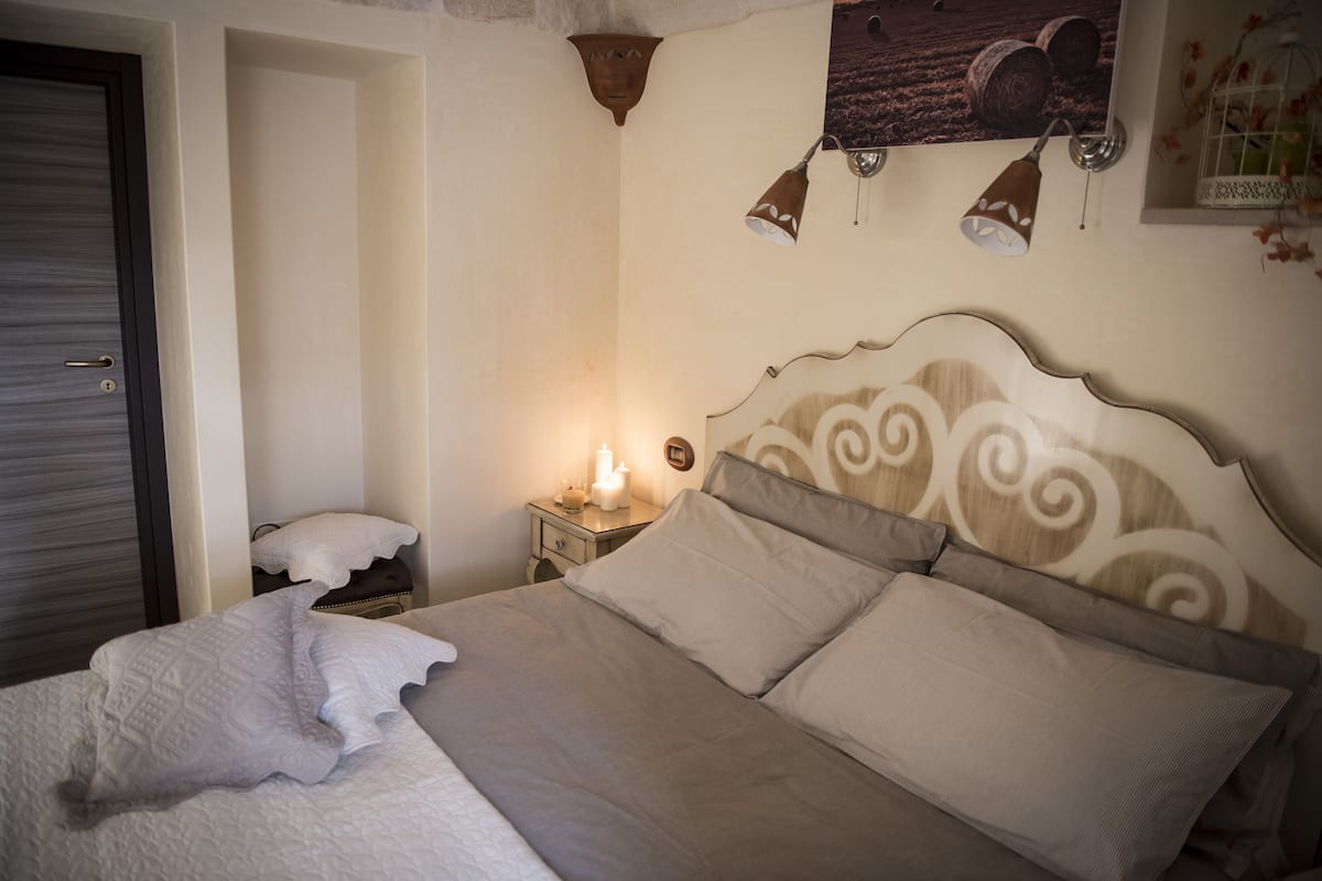 A neatly made bed with a headboard, a bedside table with a lamp, and a wall-mounted light fixture.